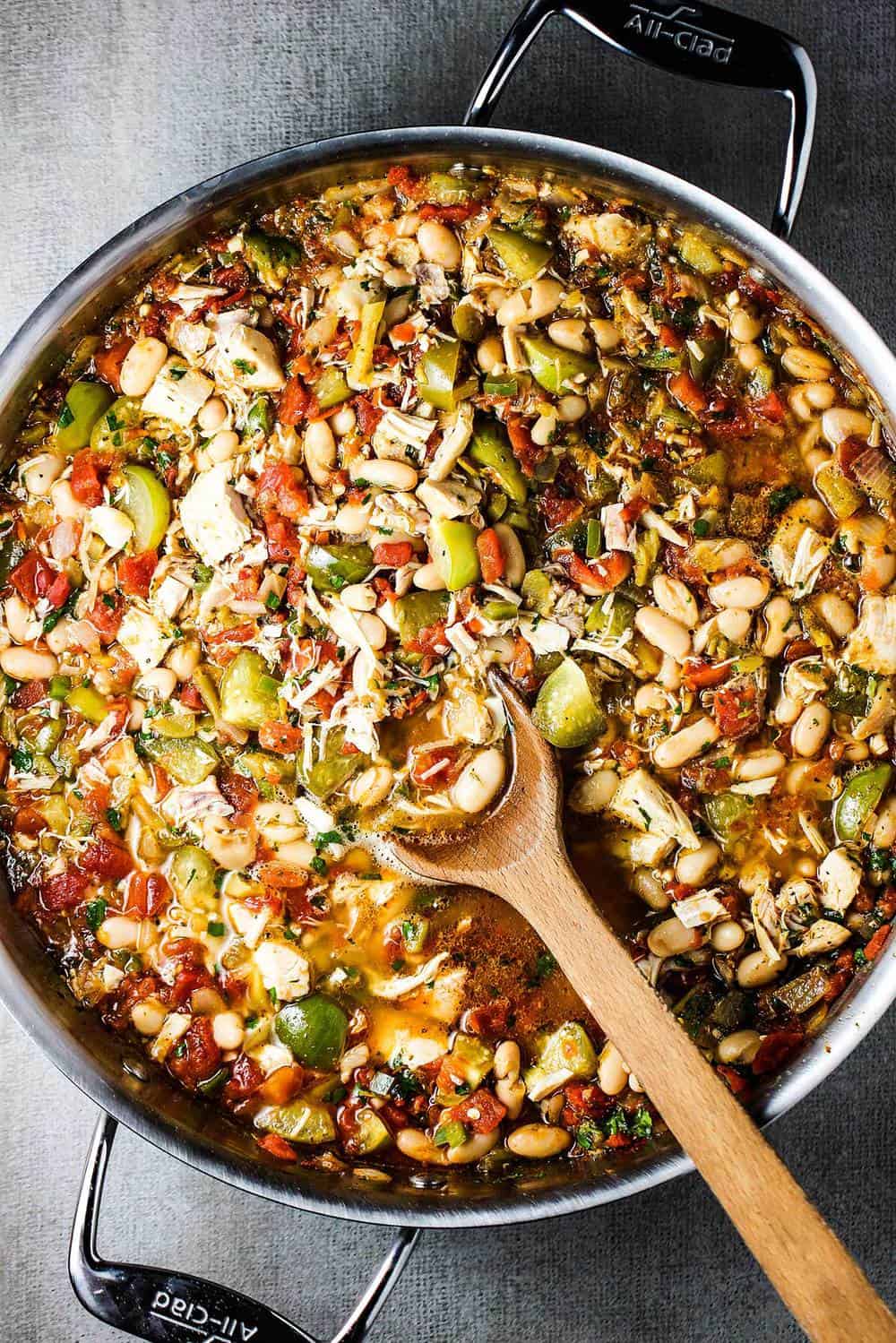 White chili with roasted tomatillos and chicken in a large skillet with a wooden spoon.