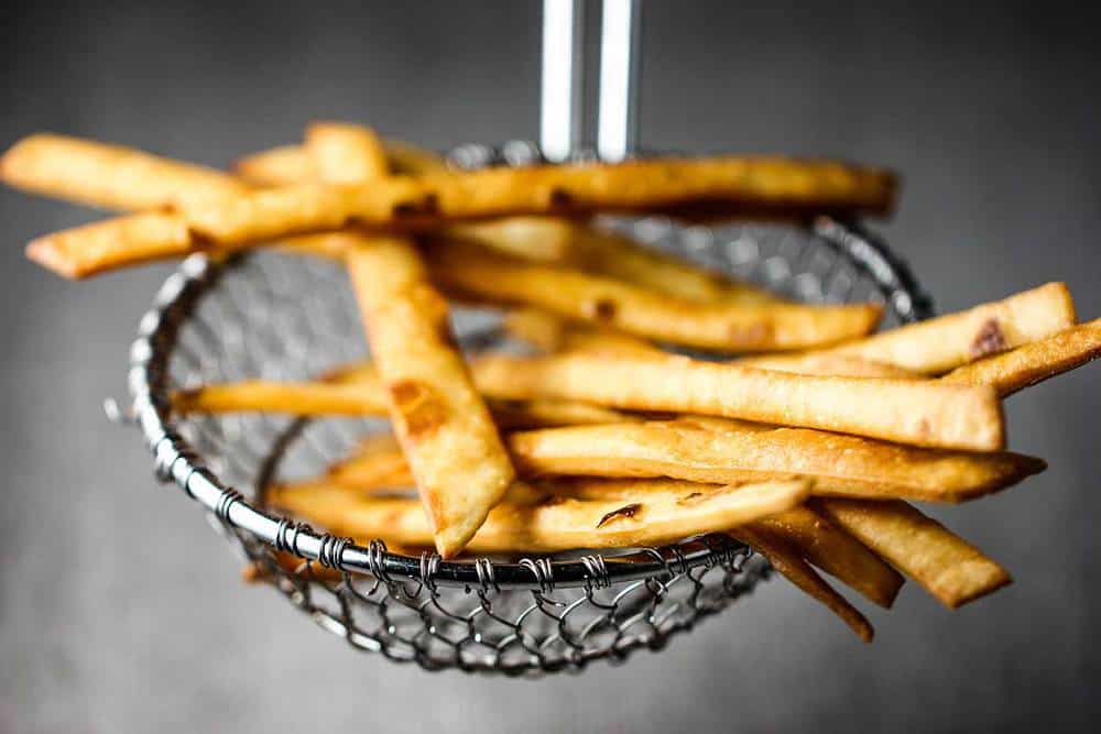 A slotted spoon holding a batch of fried flour tortilla strips.