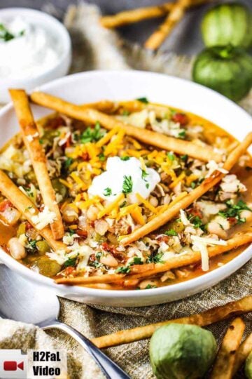 A white bowl of white chili with roasted tomatillos and chicken with a spoon next to it.