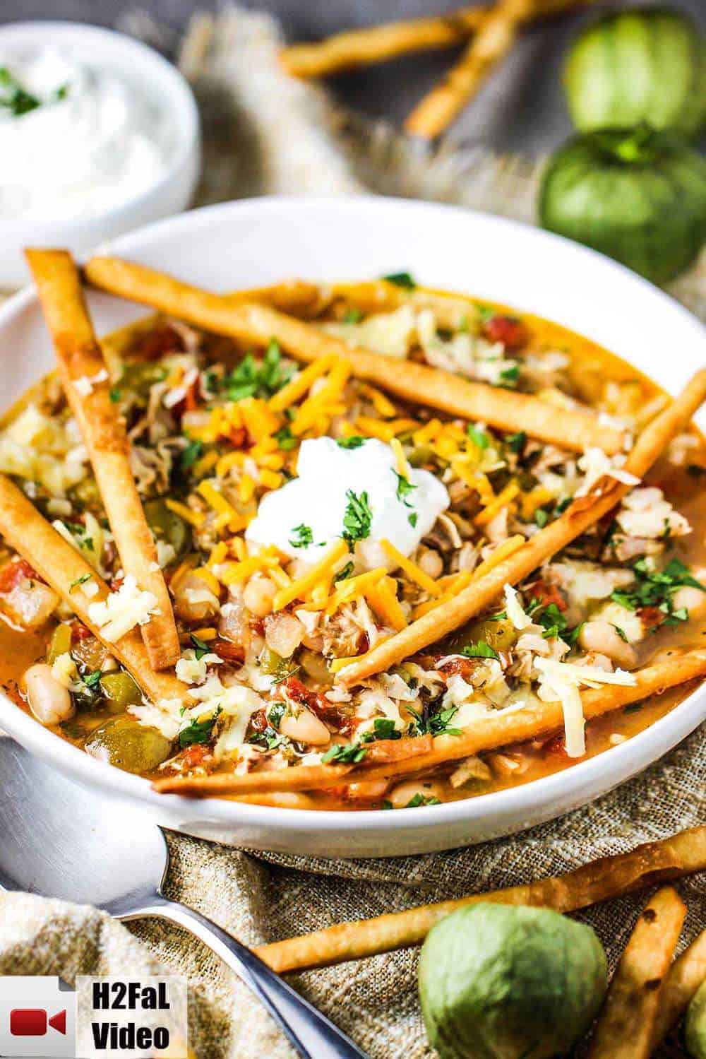 A white bowl of white chili with roasted tomatillos and chicken with a spoon next to it.