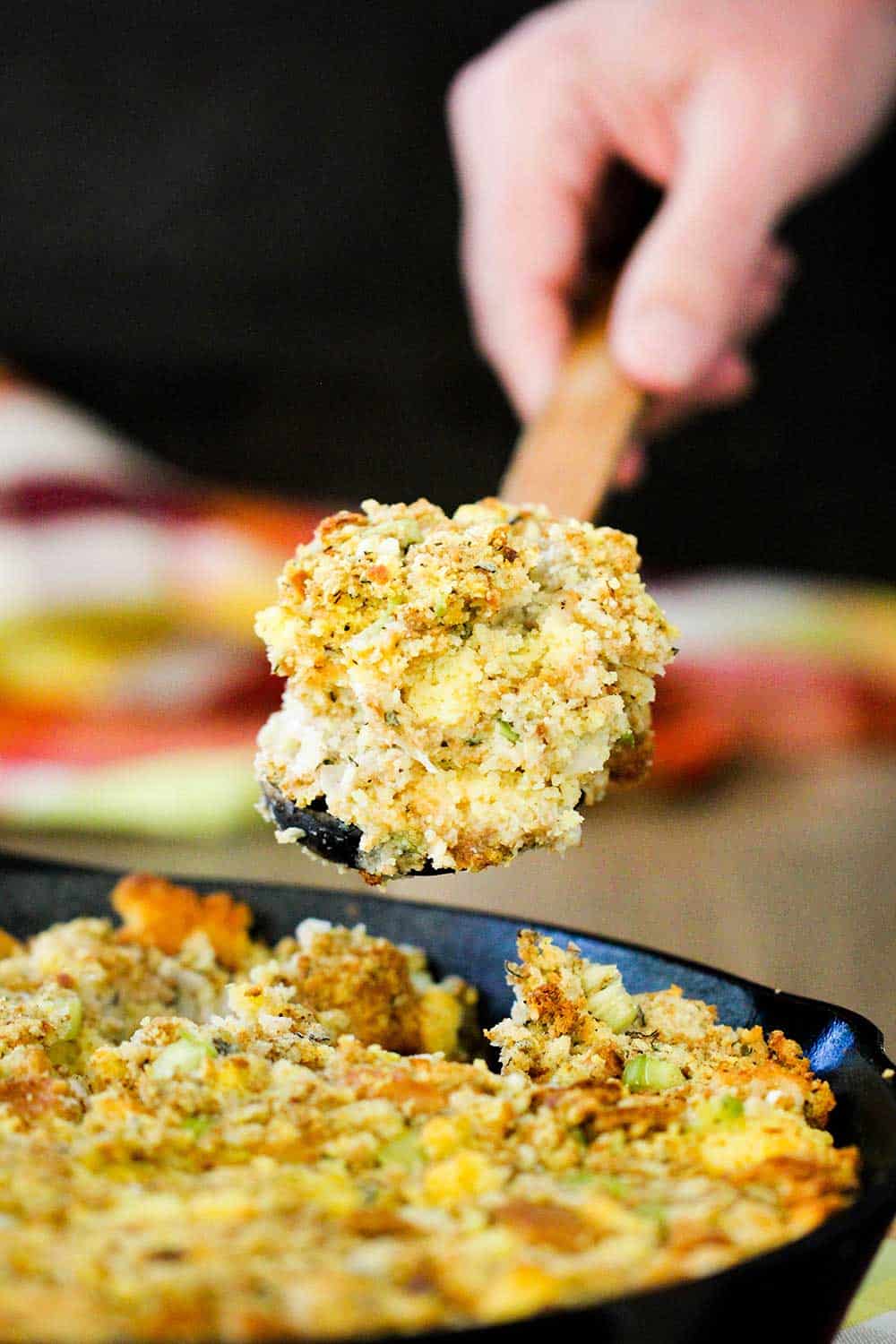 A hand holding a large spoonful of Mom's Thanksgiving Dressing over a skillet.