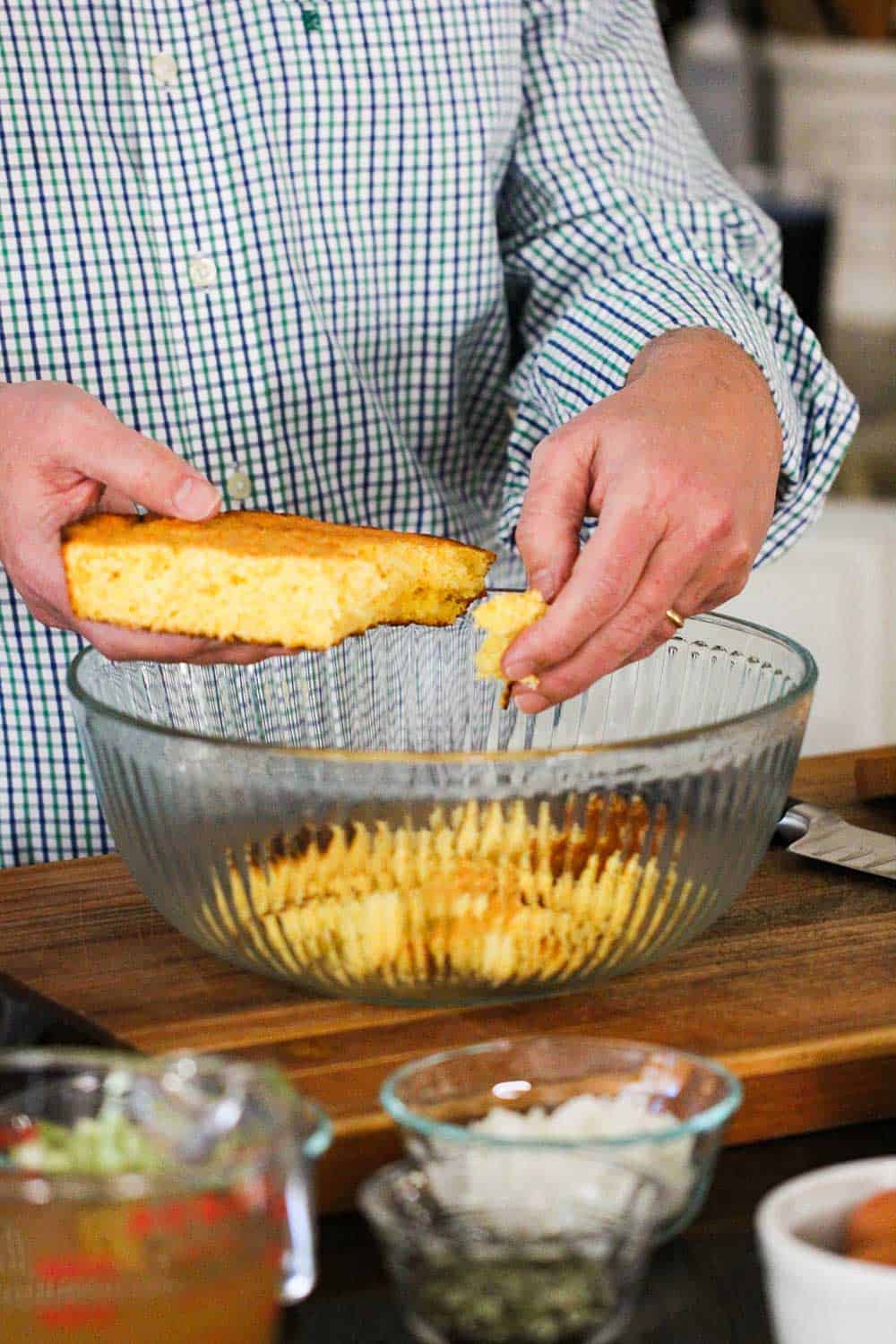 A hand crumbling in homemade cornbread into a large glass bowl.
