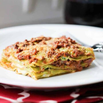 A serving of Rustic Bolognese Lasagna on a white plate on top of a red patterned place setting
