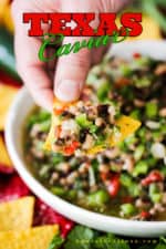 A hand holding a chip loaded with Texas Caviar over a bowl of the dip.