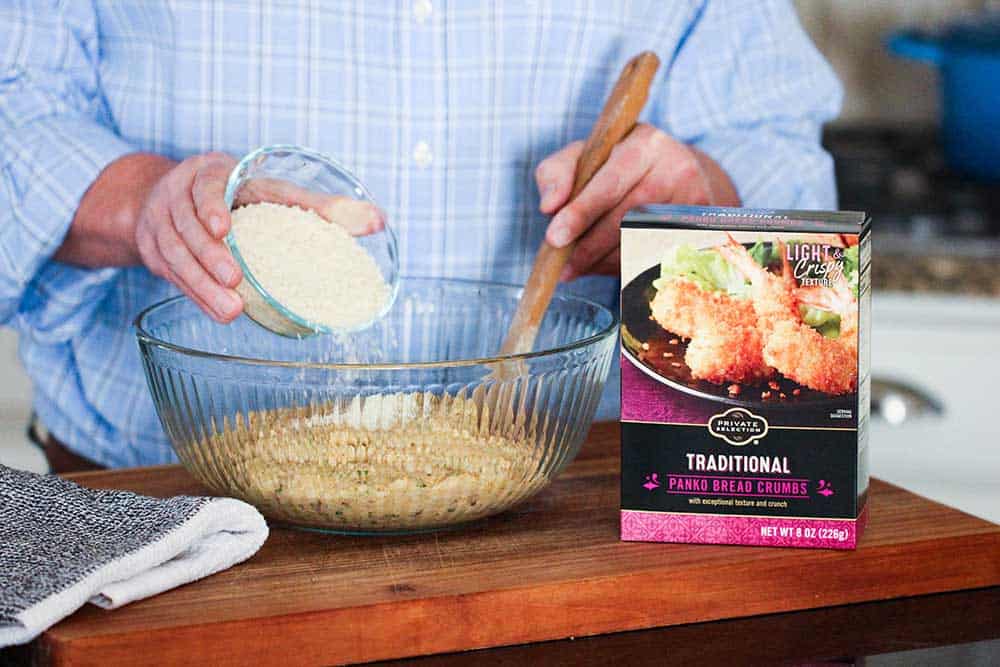 A person mixing Panko bread crumbs into a large glass bowl full of shrimp ball batter next to a box of Panko bread crumbs.