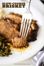 A fork cutting into a tender piece of slow-cooker brisket on a white serving plate.