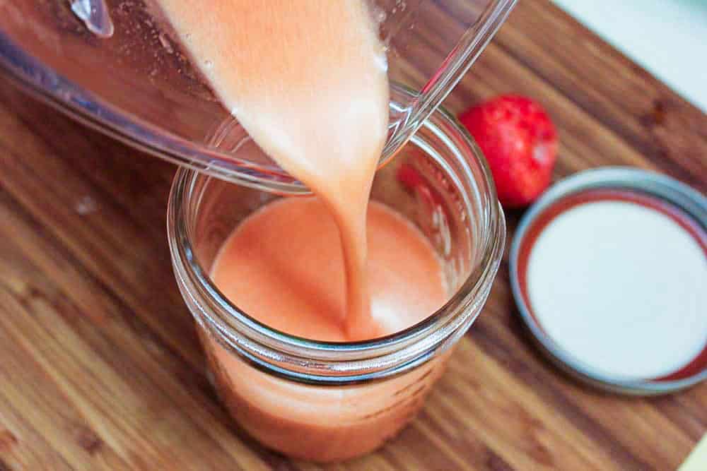 Strawberry vinaigrette being poured from a blender into a jar with its lid sitting next to it.