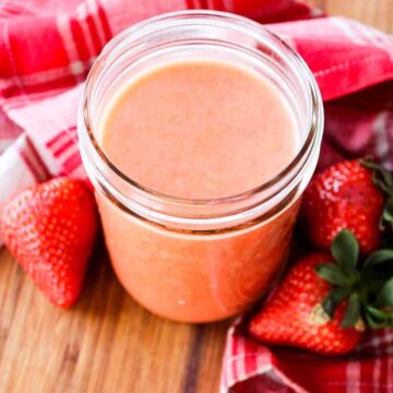 A jar of strawberry vinaigrette next to three fresh strawberries and a red napkin.