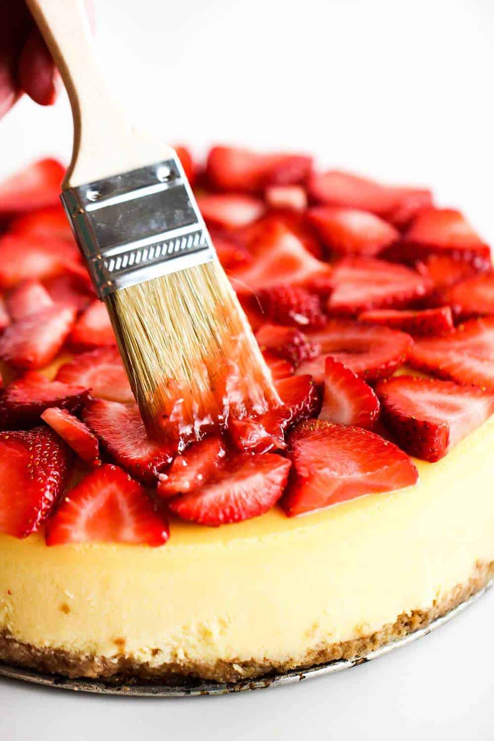 Brush applying a strawberry glaze on top of a New York cheese cake.