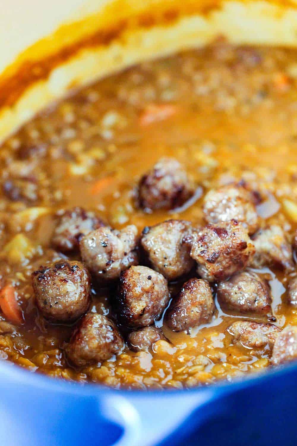 A large blue Dutch oven filled with rustic lentil soup with Italian sausage balls resting on the top.
