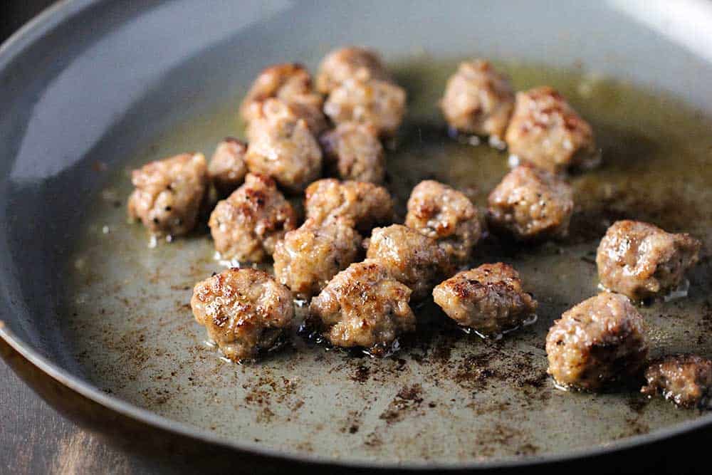 A large skillet filled with small Italian sausage balls that have been browned.