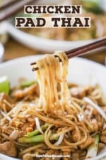 A pair of chopsticks lifting rice noodles from a bowl filled with chicken pad Thai.