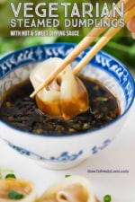 A person using two chopsticks to dunk a steamed dumpling into a small Asian bowl filled with hot and sweet dipping sauce.