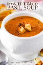 A white soup filled with roasted tomato basil soup next to sliced grilled cheese sandwiches.