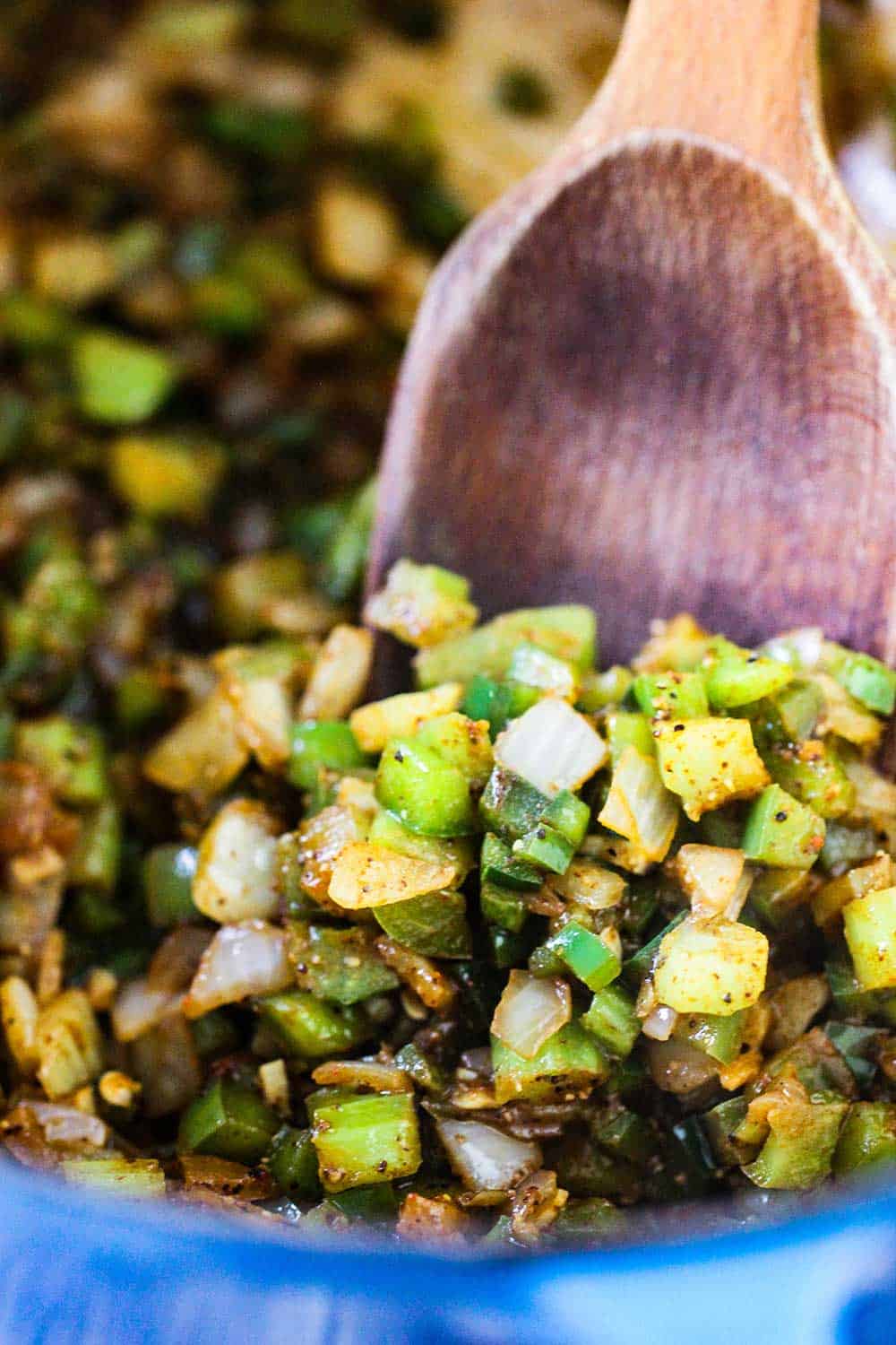 A blue Dutch oven with sautéed vegetables in it with a large wooden spoon in the middle.
