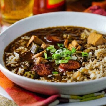 A white bowl chicken and sausage gumbo on top of patterned napkin with a spoon next to it.