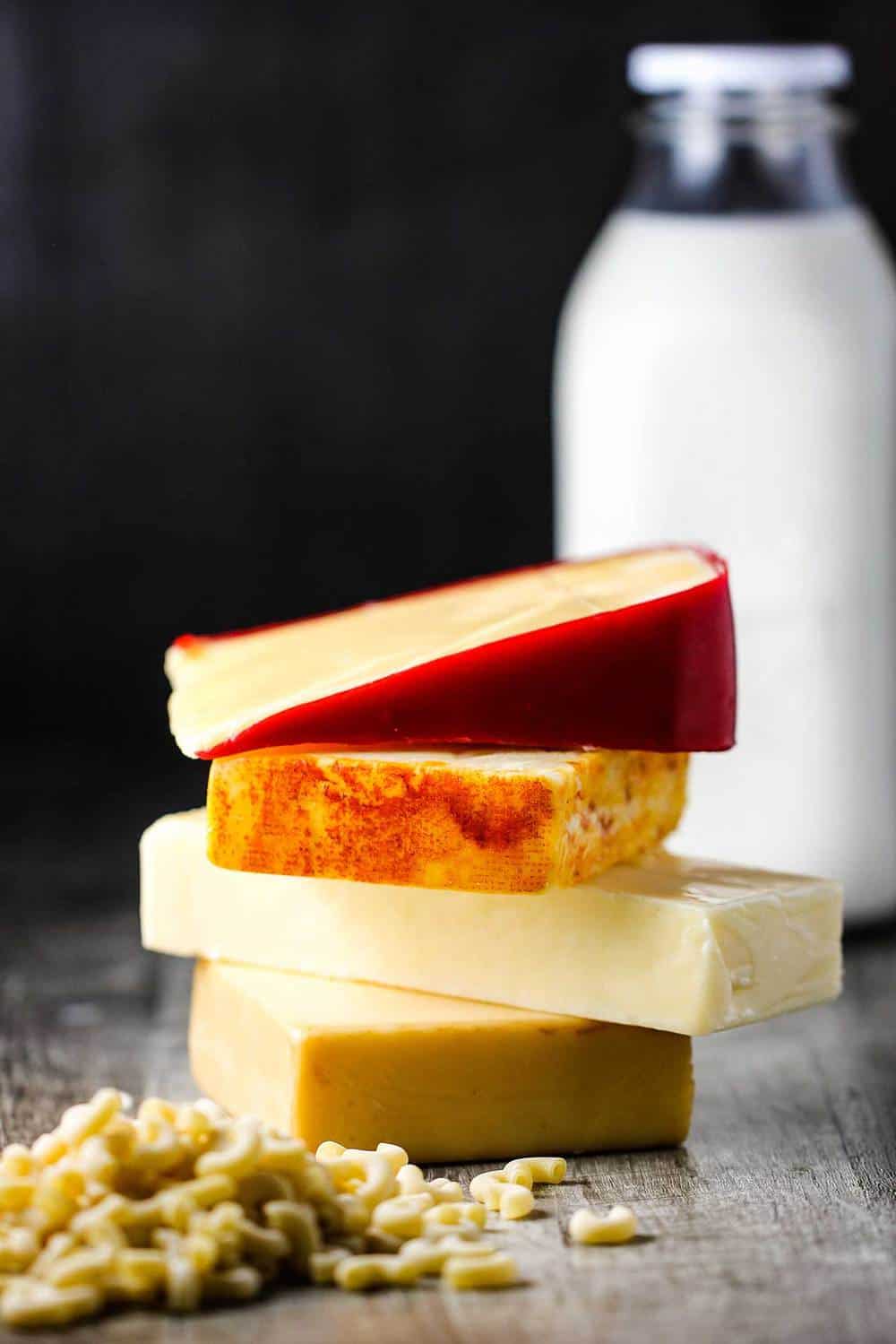 Blocks of cheese stacked next to dried macaroni and a bottle of milk.