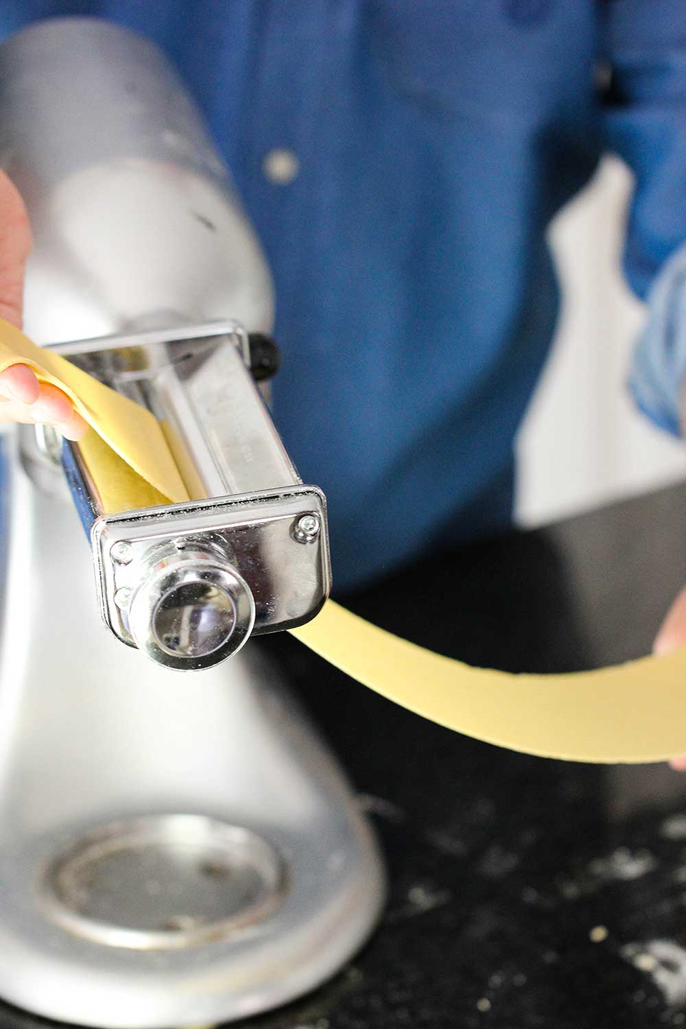 A sheet of homemade pasta being put through a pasta roller on a stand mixer.
