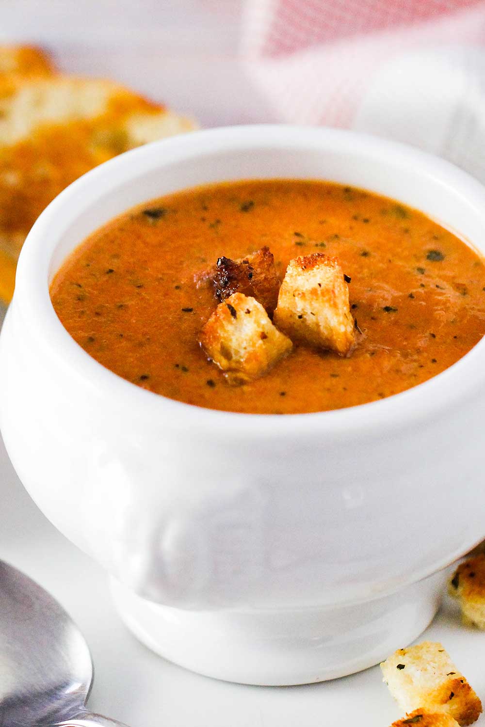 A white bowl of roasted tomato basil soup with croutons on top.