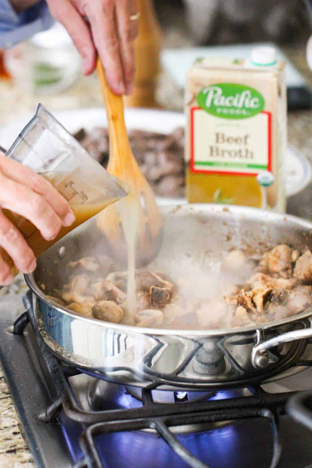 Beef broth being poured into a skillet of gourmet beef stroganoff.