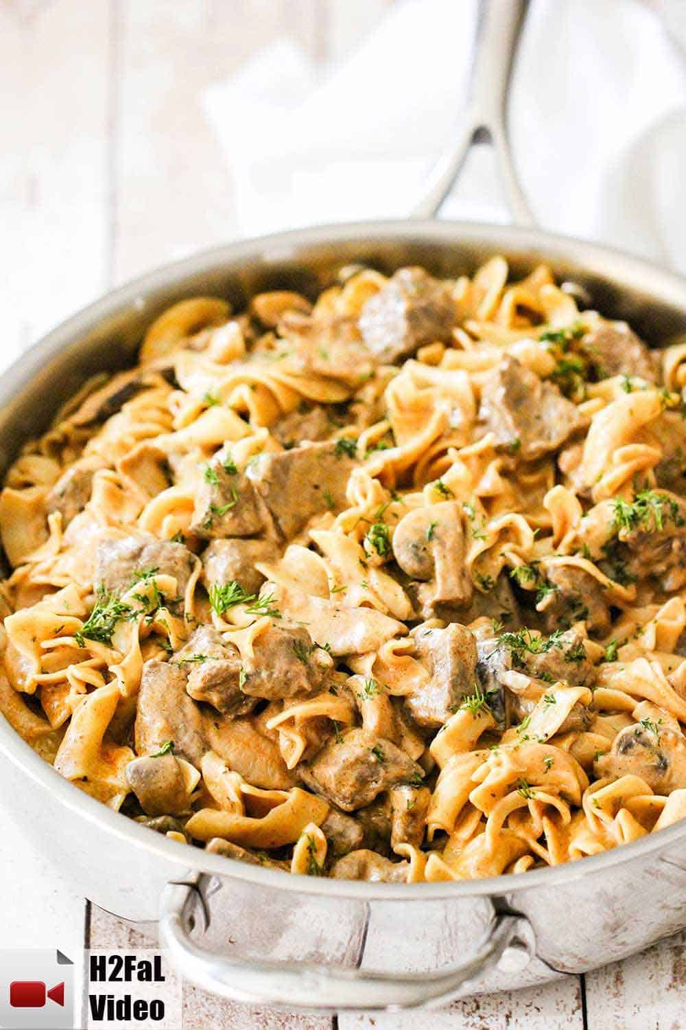 A large skillet containing gourmet beef stroganoff on a white background.