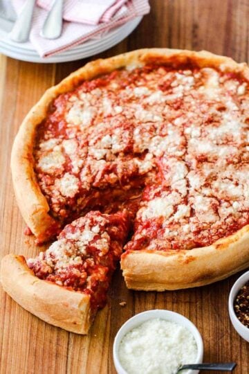 A Chicago-Style Deep Dish Pizza on a cutting board with a slice pulled out next to Parmesan cheese.