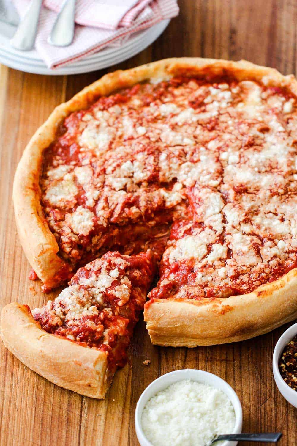 A Chicago-Style Deep Dish Pizza on a cutting board with a slice pulled out next to Parmesan cheese.