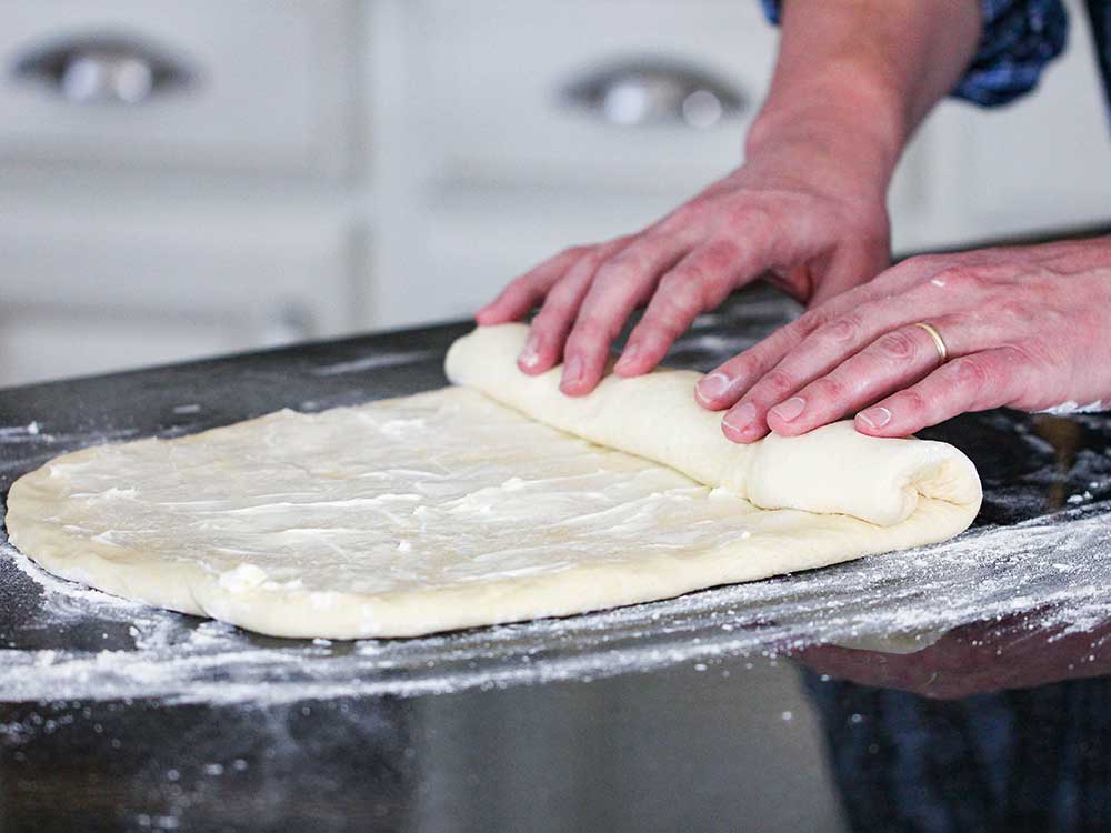Two hands rolling pizza dough on a floured surface.