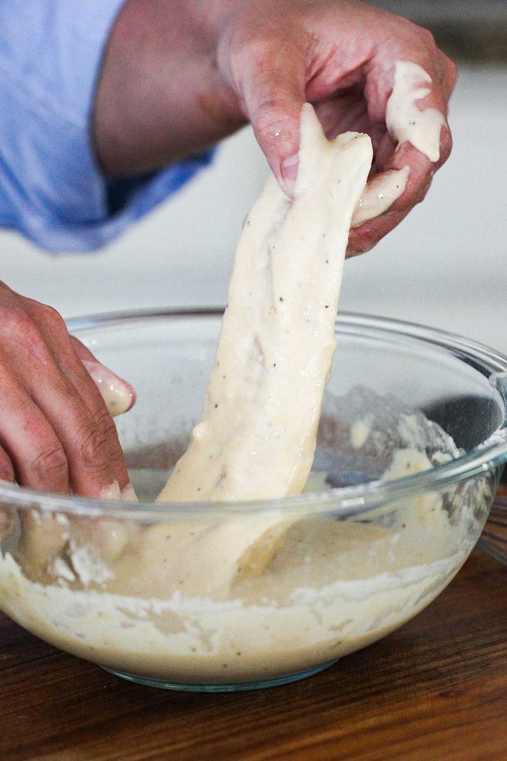 A filet of cod being dipped into a bowl of batter for fish and chips.