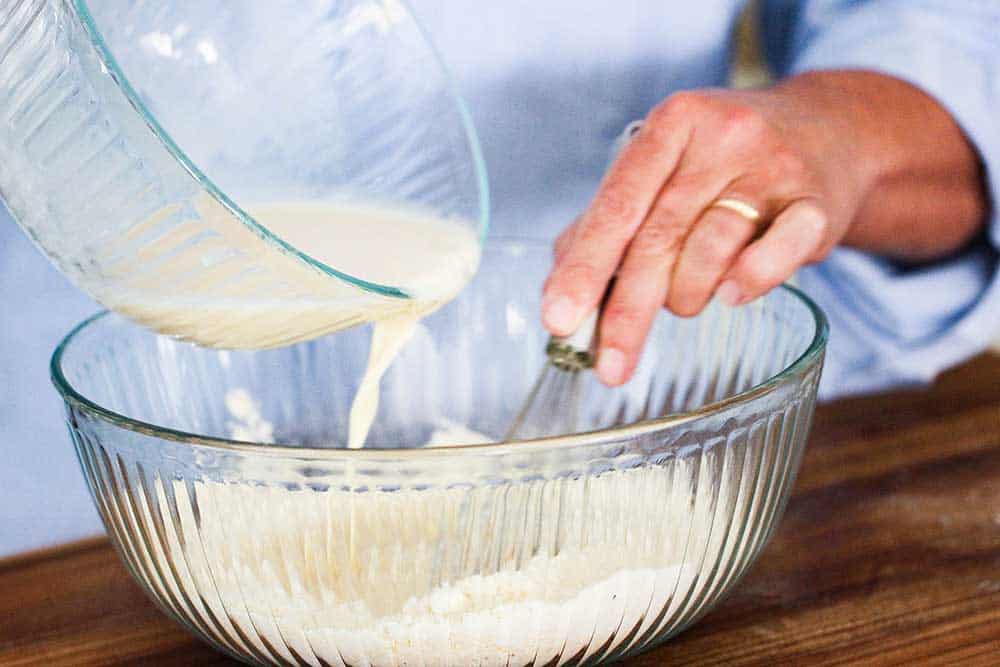 A bowl of wet ingredients being poured into a bowl of dry ingredients for batter.