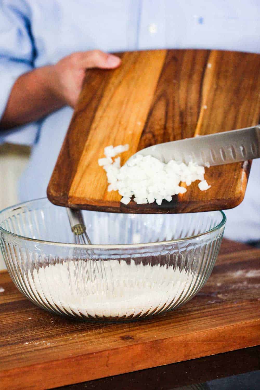 Chopped onions being scraped into a bowl of hush puppies batter.