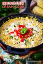 A cast-iron skillet filled with Mexican cream corn topped with crumbled queso fresco, chopped tomatoes, and chopped cilantro.