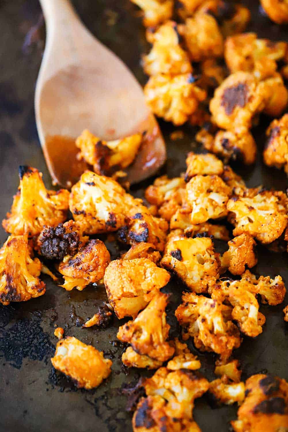 A baking dish filled with buffalo cauliflower bites with a wooden spoon inserted in the middle of them.
