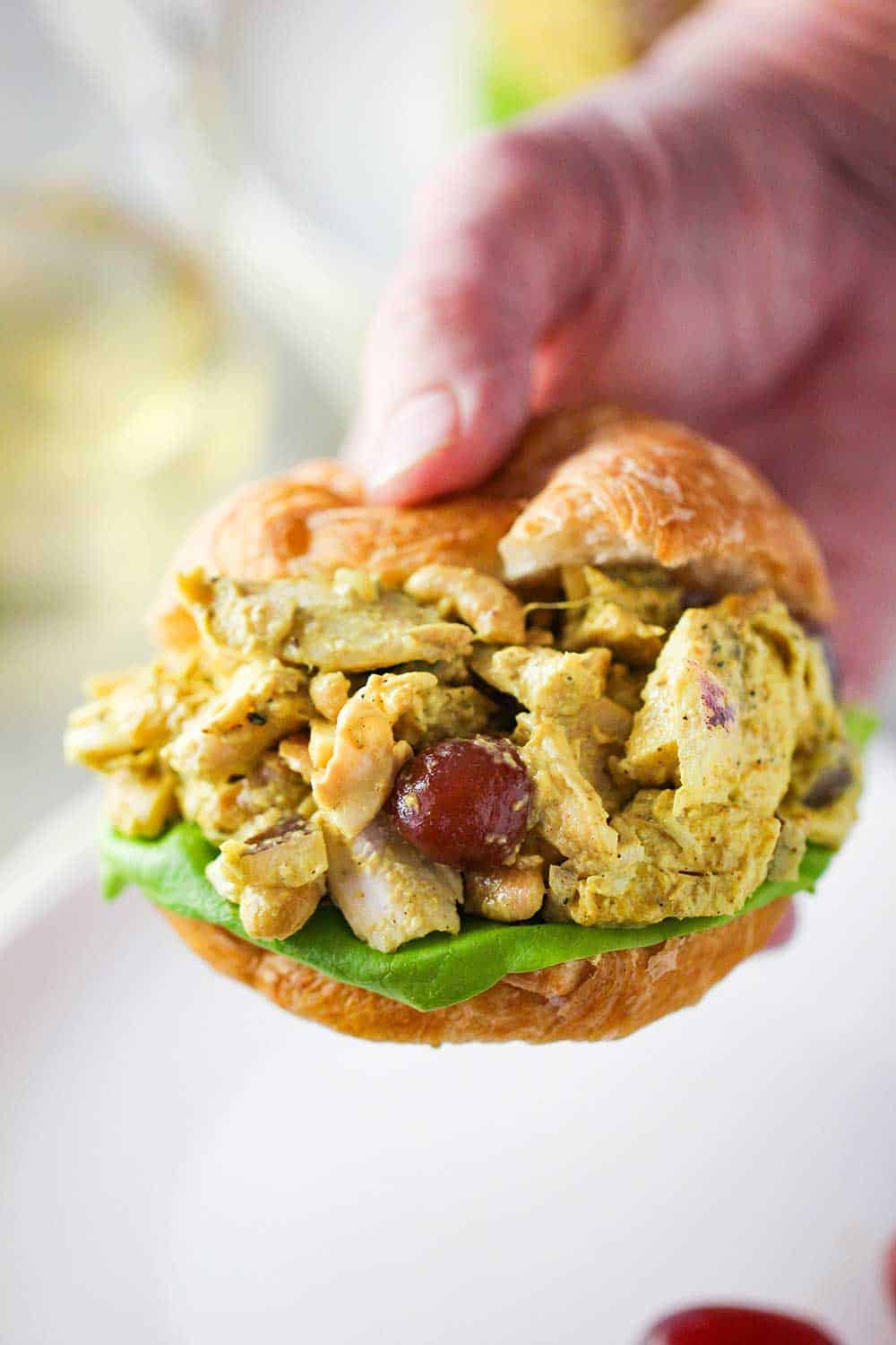 A hand holding a sandwich of curry chicken salad between to croissant halves.