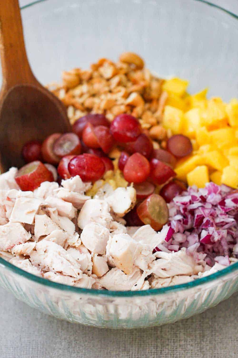 A large glass bowl of cooked cubed chicken, grapes and mango for chicken salad.