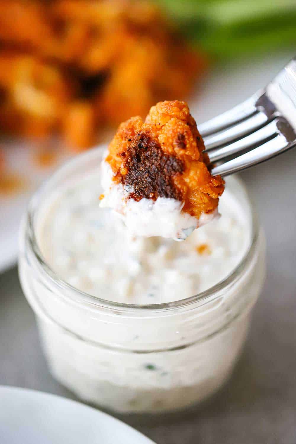 A buffalo cauliflower bite stuck on the end of a fork and being dipped into a small bowl of blue cheese dressing.