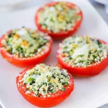 An overhead view of four large tomatoes that have been split in half and roasted with bread crumbs in the cavity.