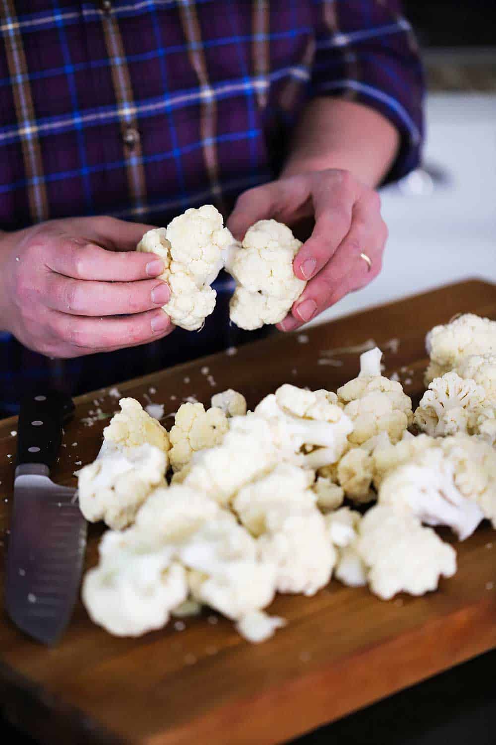 A person pulling apart cauliflower florets on a large wooden cutting board.
