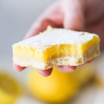 A person holding a lemon bar with a bit taken out of the corner of it.