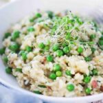 A white individual bowl filled with risi e bisi and topped with pea shoots.