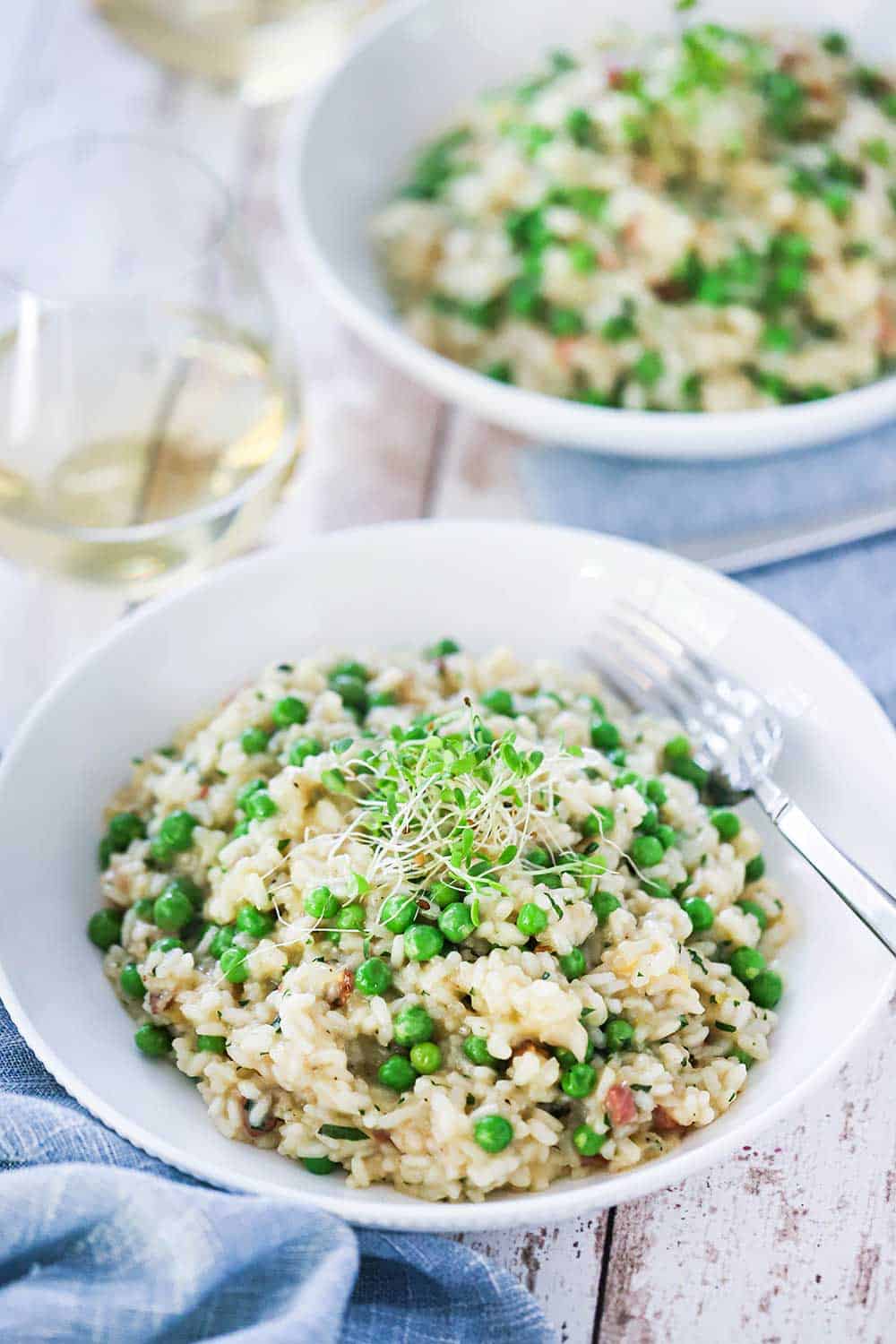 A white individual bowl filled with risi e bisi and topped with pea shoots.