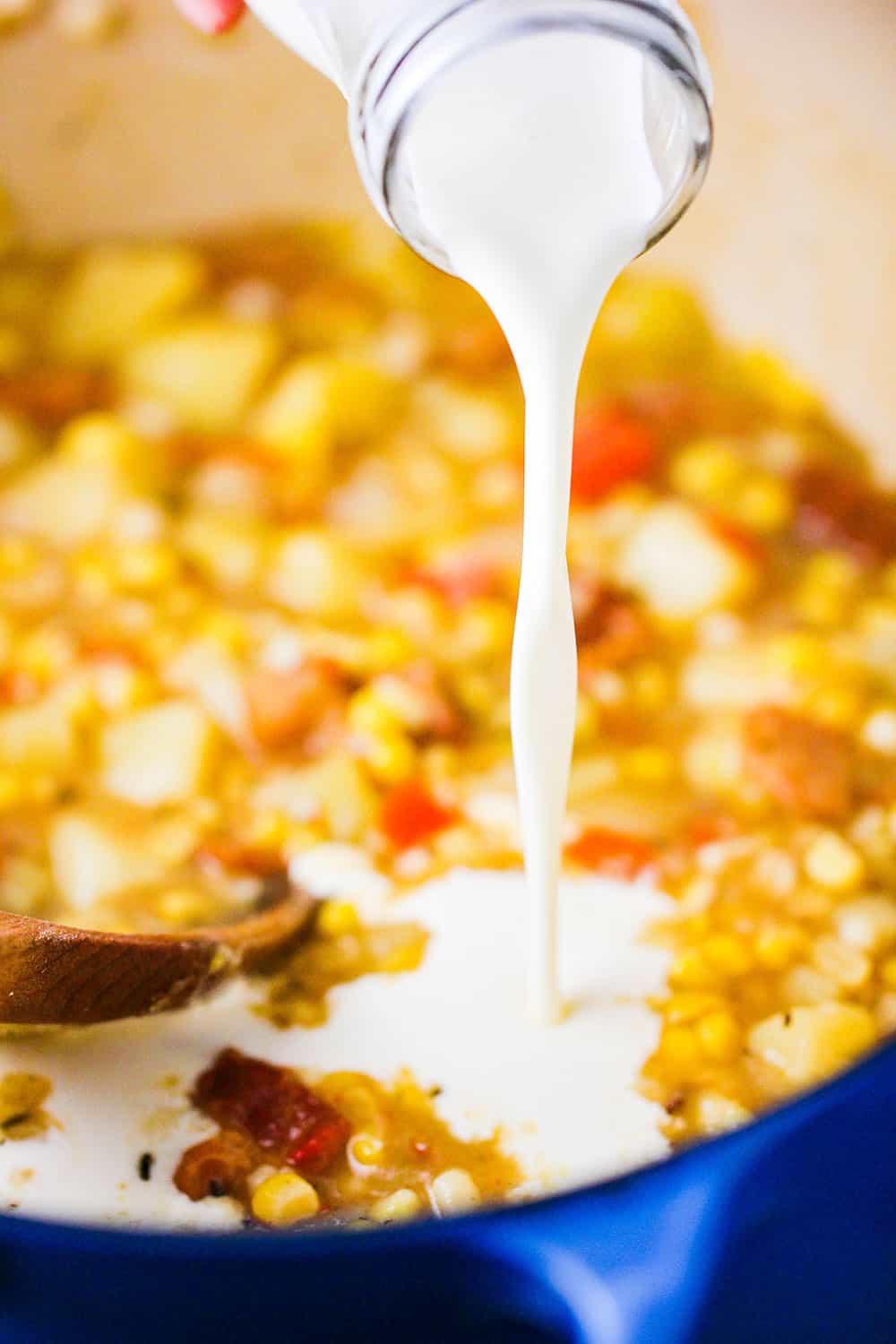 A dairy bottle of cream being poured into a large pot of farm fresh corn chowder.