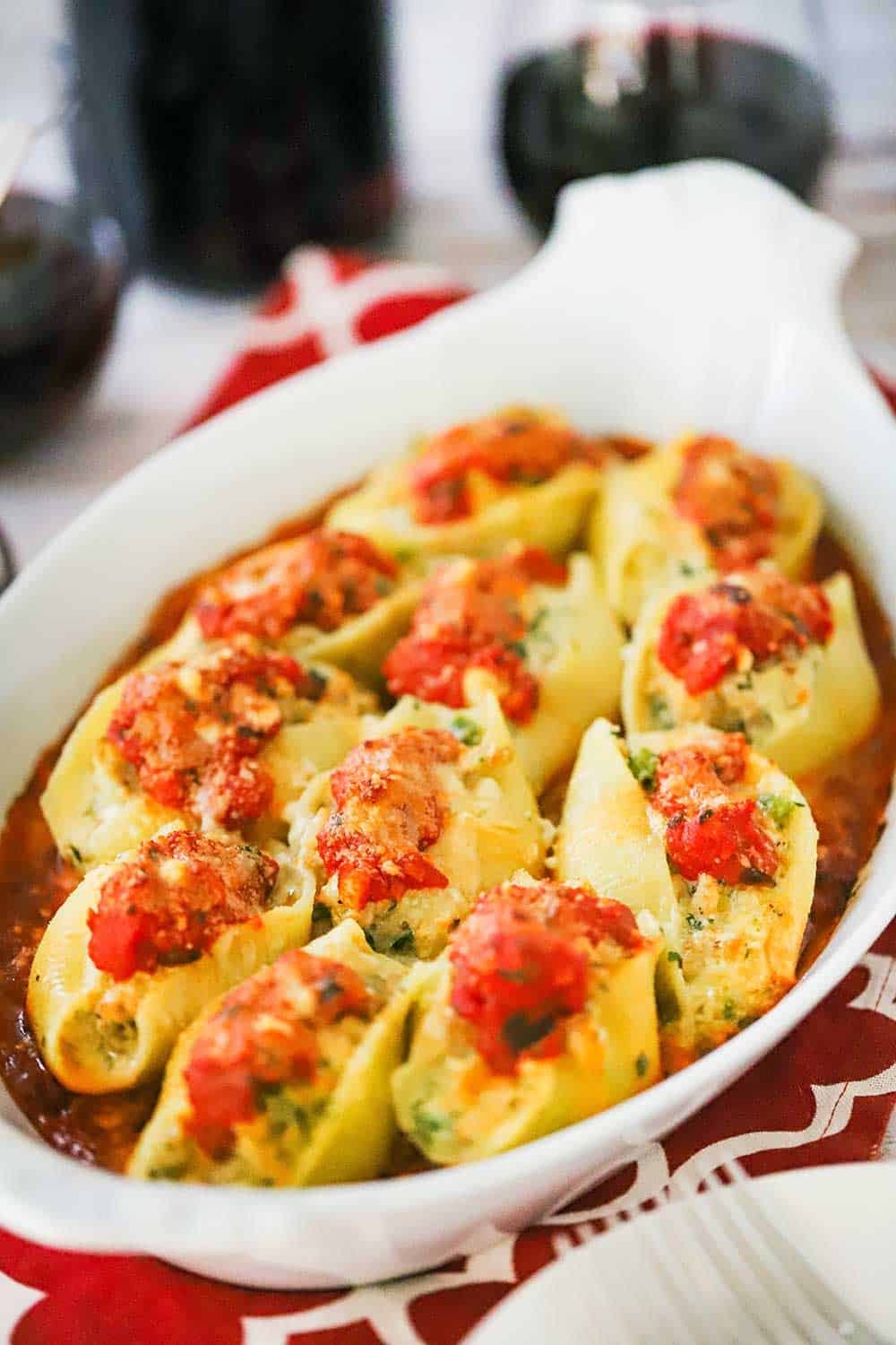 An oval white baking dish filled with cooked Italian stuffed shells all sitting on a layer of marinara sauce.