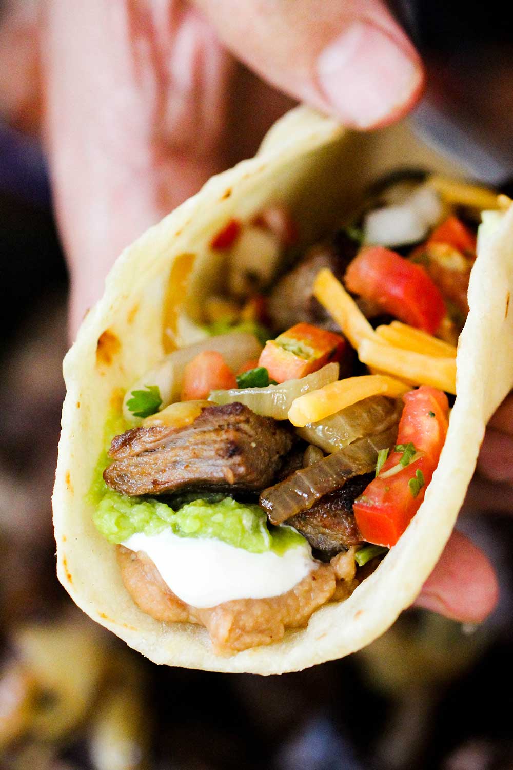 A hand holding an authentic steak fajita filled with beans, guacamole, sour cream, steak and pico de gallo.