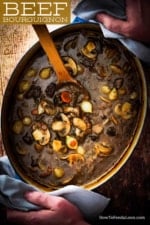 A large oval Dutch oven filled with beef bourguignon being held by two hands.
