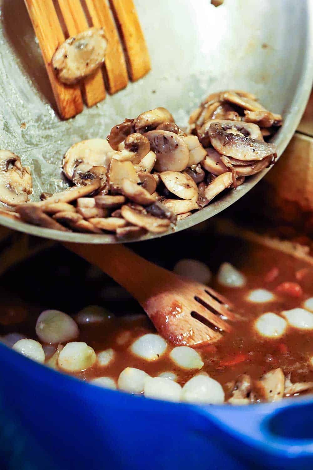 Sautéd mushrooms being transferred into a pot of simmering beef bourguignon.