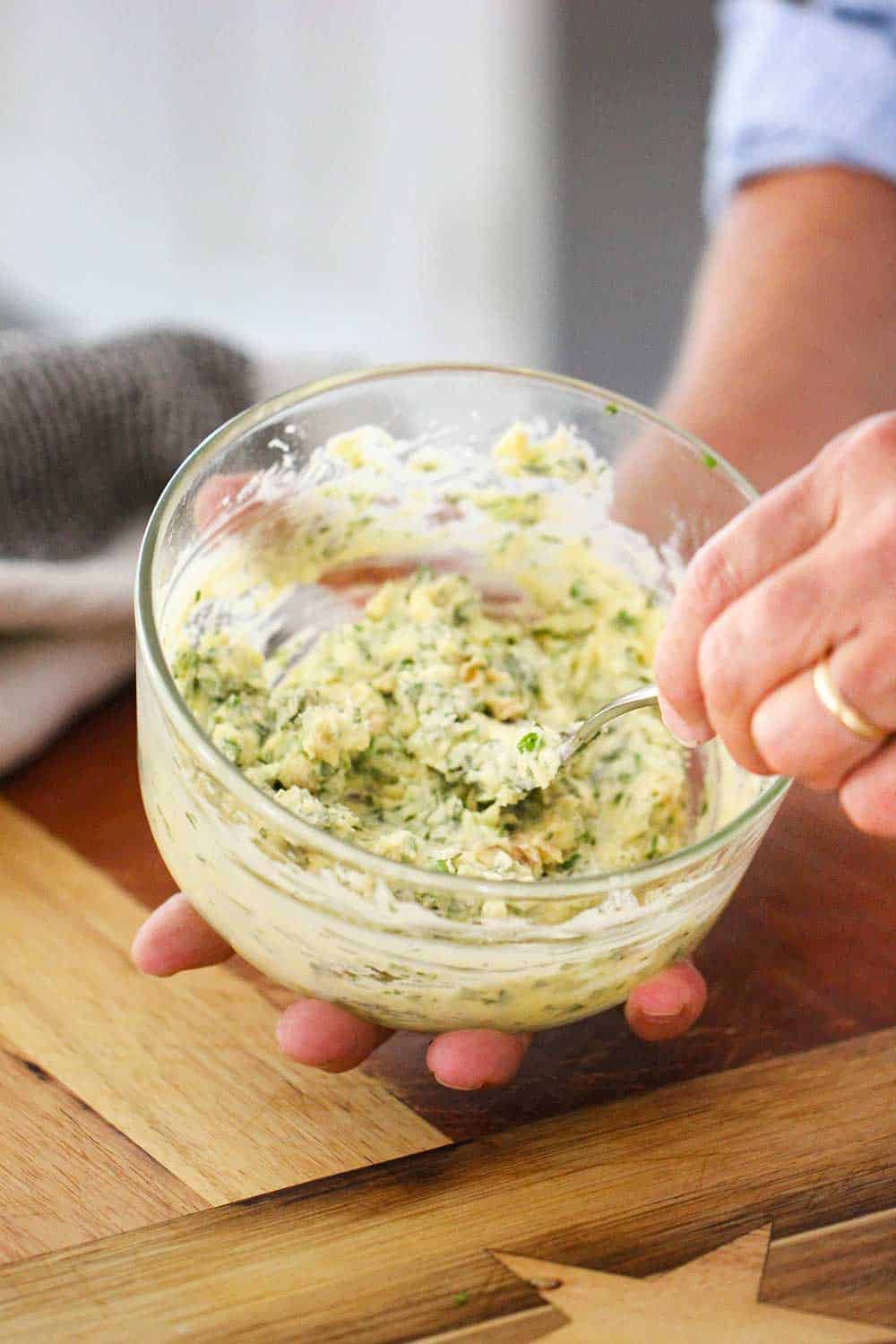 A hand mixing together a butter, herb and garlic mixture for cheesy garlic bread.