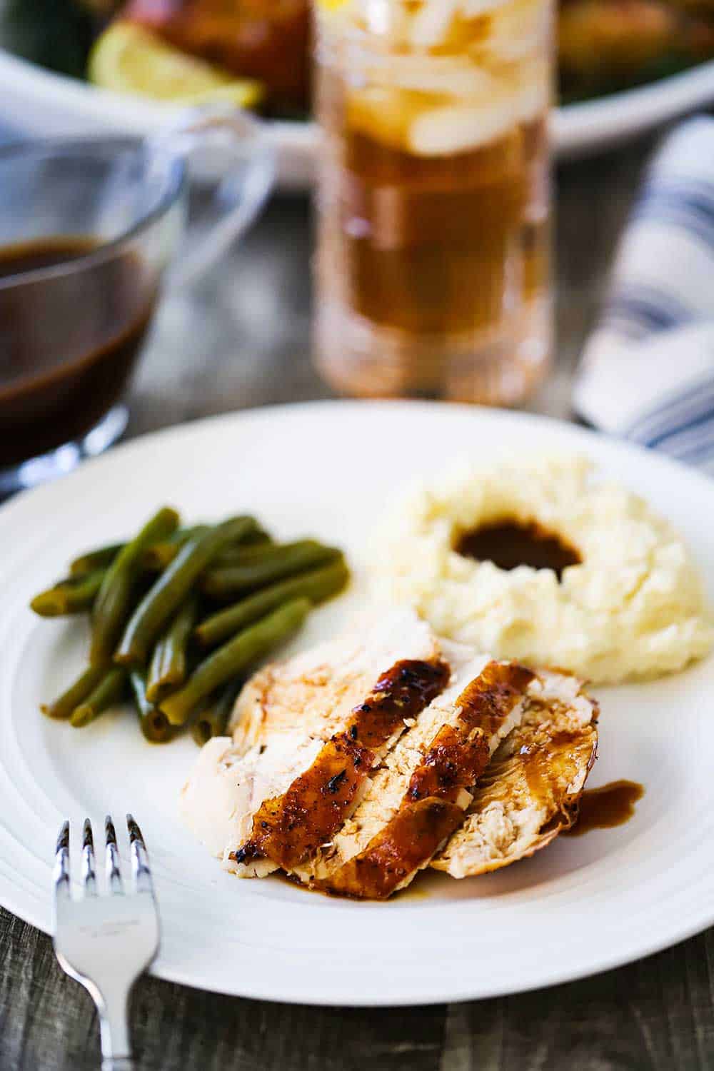 A white dinner plate filled with sliced roasted chicken, mashed potatoes and gravy, and green beans.
