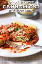 A close-up view of a half eaten spinach and cannelloni with meat sauce on the top and a fork resting on the plate.