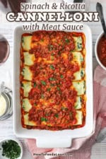 An overhead view looking straight down on a white 9 by 13 baking dish that is filled with spinach and ricotta cannelloni topped with a tomato-based meat sauce.